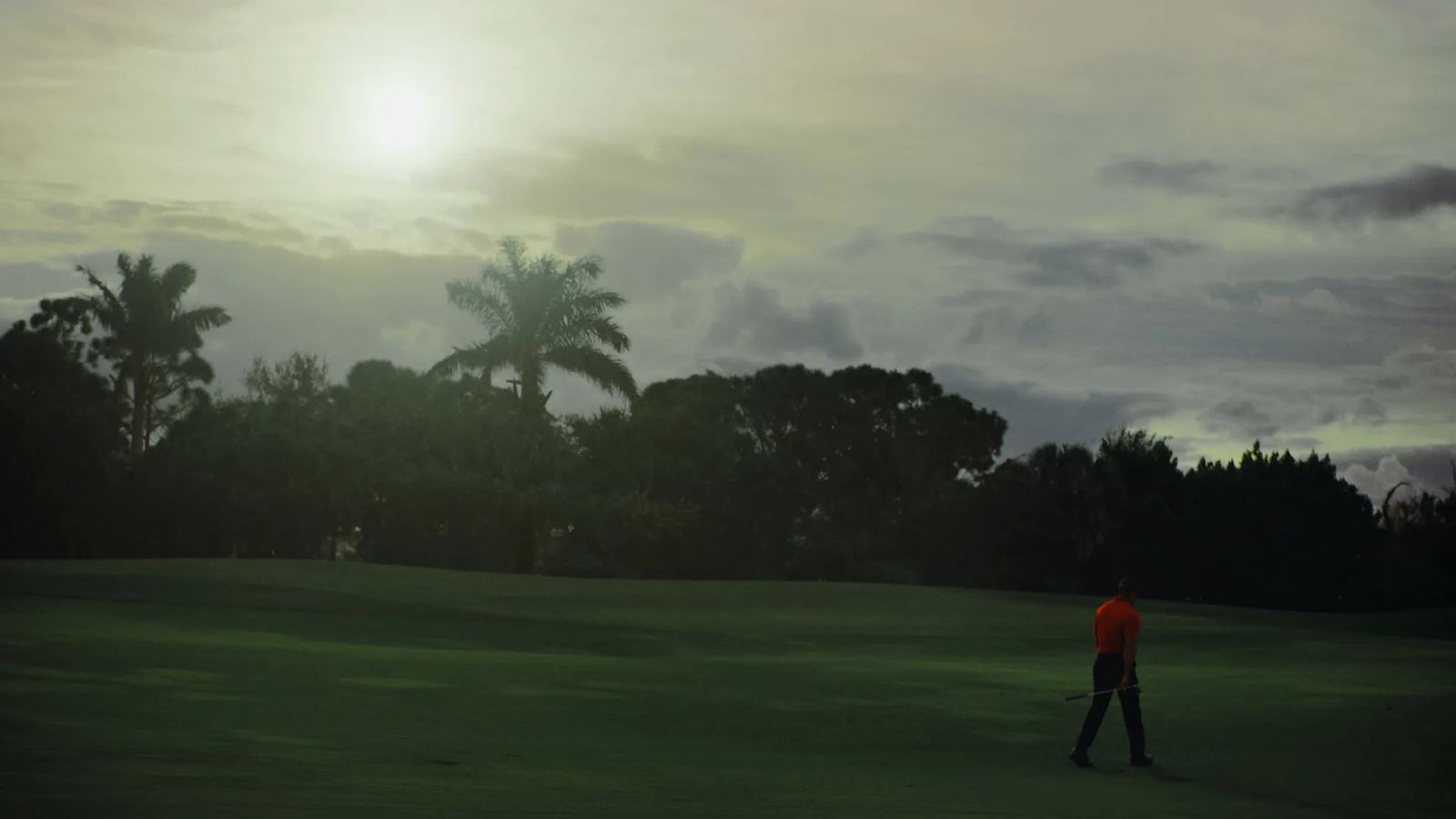A lone golfer in a red shirt on a fairway at dusk